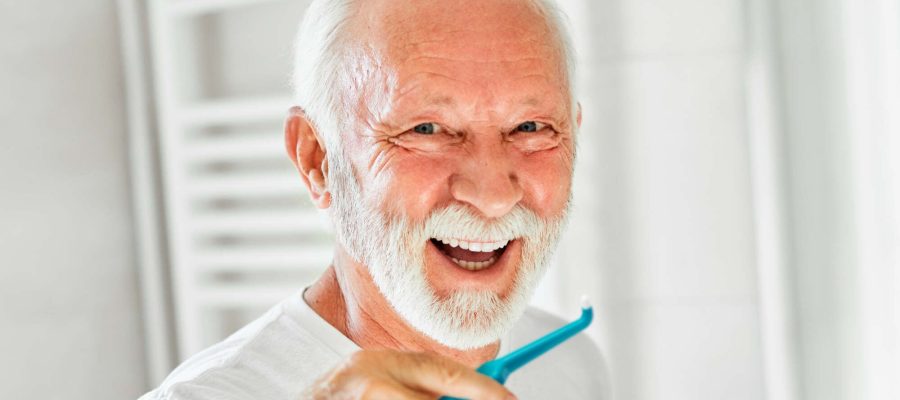 Portrait of an elderly senior man is cleaning brushing his teeth in front of mirror in bathroom. Dental hygiene, vitality and beauty concepts